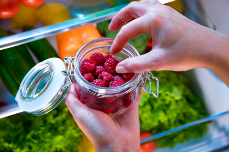 Woman takes the fresh raspberries berry from the open refrigerator. Healthy food.の写真素材