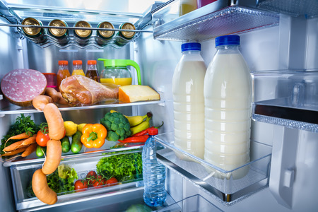 Open refrigerator filled with food. Focus on Bottles of milk in the fridgeの写真素材