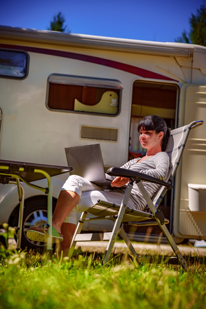Woman looking at the laptop near the camping . Caravan car Vacation. Family vacation travel, holiday trip in motorhome. Wi-fi connection information communication technology.の写真素材