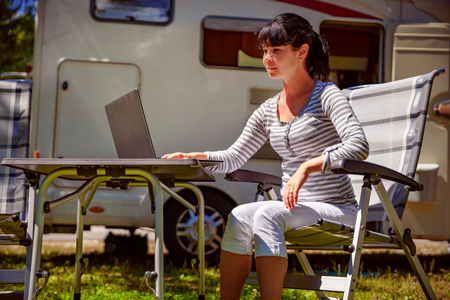 Woman looking at the laptop near the camping . Caravan car Vacation. Family vacation travel, holiday trip in motorhome. Wi-fi connection information communication technology.の写真素材