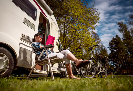 Woman relaxes and reads a book near the camping . Caravan car Vacation. Family vacation travel, holiday trip in motorhome.の写真素材