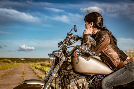 Biker girl in a leather jacket and sunglasses sitting on motorcycleの写真素材