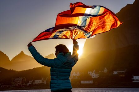 Woman waving the flag of Norway at sunset