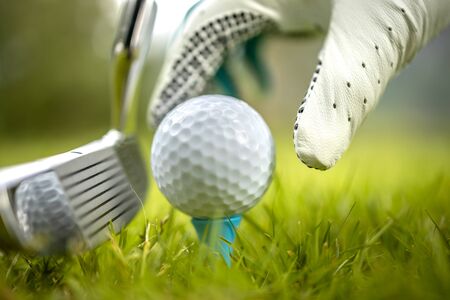 Hand in glove placing golf ball on tee