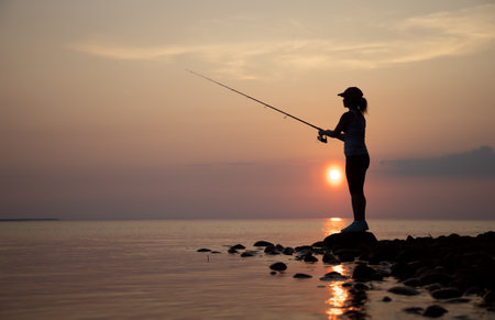 Woman fishing on Fishing rod spinning in Finland at sunset.の写真素材