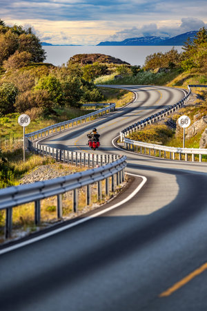 Couple rides a motorcycle on a winding Atlantic road in Norway. Atlantic Ocean Road or the Atlantic Road (Atlanterhavsveien) was awarded the title as "Norwegian Construction of the Century"の写真素材