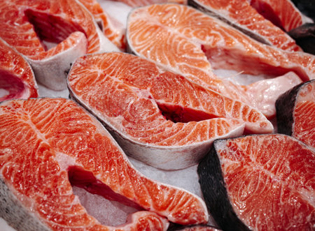 Fresh raw salmon steaks on display, bright orange fish meat with marble texture and skin, ready for...