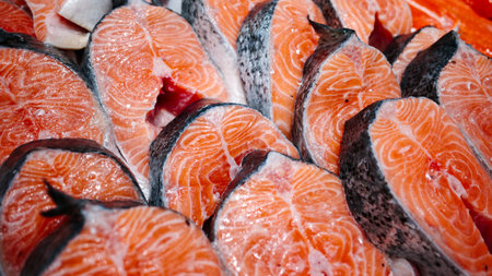 Fresh raw salmon steaks on display, bright orange fish meat with marble texture and skin, ready for cooking, seafood market background.