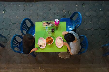 Top view two people to eating enjoy with Thailand street food spicy soup and rice on the road street in the Bangkok city. They are coupled.の写真素材