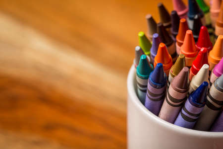 Crayons in a white mug sitting on a wooden desk.の写真素材