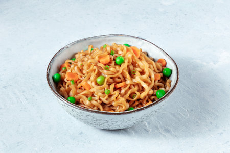 Instant noodles in a bowl, with green peas and carrotsの写真素材