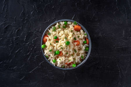 Rice with vegetables, shot from above on a dark black background