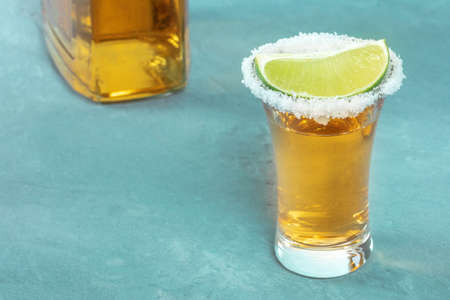 Tequila shot with a lime slice and a bottle, a Mexican drink with a salt rim, with a bottle and copy spaceの写真素材