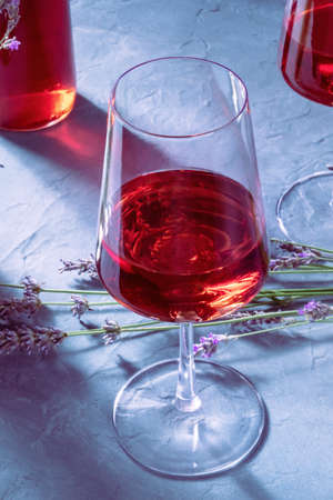 Rose wine close-up with another glass, a bottle, and a bunch of fresh lavender flowers in the background, a still life with shadowsの写真素材