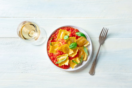 Ravioli with tomato sauce and fresh basil leaves on a plate, Italian pasta dish, shot from the top on a rustic wooden background with white wineの写真素材