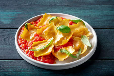 Ravioli with tomato sauce and fresh basil leaves on a plate, Italian pasta dish, on a dark rustic wooden backgroundの写真素材