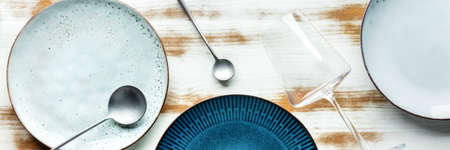 Modern tableware panorama with a vibrant blue plate, cutlery, and a wine glass, overhead flat lay shot. Trendy dinnerware on a rustic backgroundの写真素材