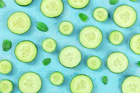 Fresh cucumber slices and mint leaves on a blue background, overhead flat lay shot. Healthy organic eating patternの写真素材