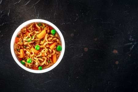 Ramen cup, instant soba noodles in a plastic cup with vegetables, shot from above with a place for text on a black stone backgroundの写真素材