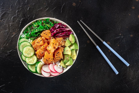 Salmon poke bowl with avocado, cucumbers, wakame, radish, and purple cabbage, a healthy Hawaiian dish with rice, overhead flat lay shotの写真素材
