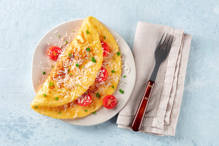 An omelet with tomato and parsley, eggs for breakfast, a healthy vegetarian dish with cheese, overhead flat lay shot with a forkの写真素材