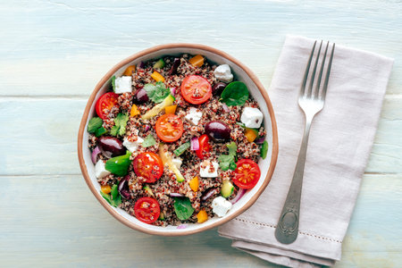 Quinoa salad, healthy Mediterranean lunch with fresh organic vegetables, cheese, and olives, top shot on a wooden background with a spoonの写真素材