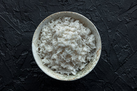 White rice, cooked. A bowl of boiled long grain rice, a simple side dish, shot from above on a black...