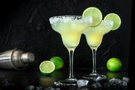 Margarita cocktails in the classic glasses, side view on a black background, with ice, lime slices and a salt rim. Summer cold drinkの写真素材
