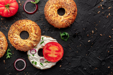 Vegetarian bagels with tomato and onions, overhead flat lay shot on a black background, with copy...