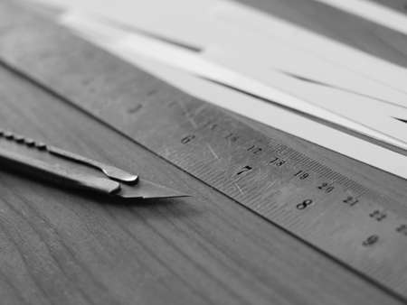 Cutter knife with stainless ruler and strip of white paper in black and whiteの写真素材