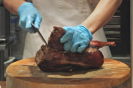 Man hand wear blue rubber glove holding Grill Roasted Peking Duck and cleaver on round wooden...