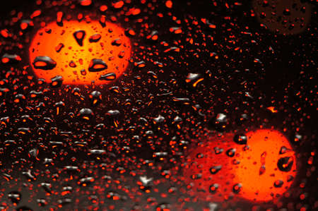 Blurred drop of rain on transparent glass window surface against colorful bokeh from street light for abstract backgroundの写真素材