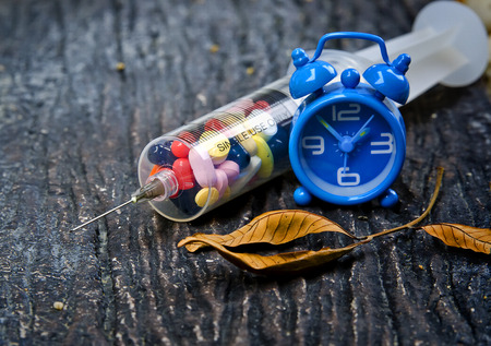 syringe full with pills and blue clock on nature backgroundの写真素材
