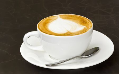 White cup of latte art on black table.