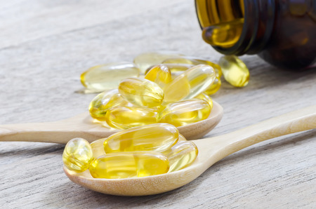 Fish oil capsules in wooden spoon on wooden background.の写真素材