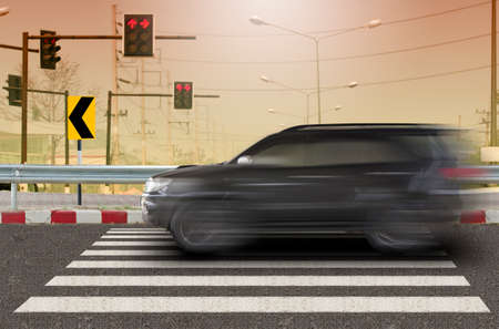 Black car driving at high speeds crossing over the crosswalkの写真素材