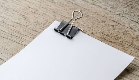 White paper with black clip on wooden background.の写真素材