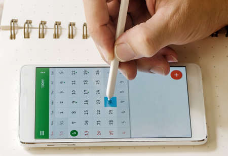 Hand holding stylus point on smartphone on blank page of note book.の写真素材
