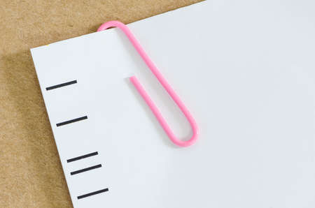 White paper with pink paper clip   on brown paper background.の写真素材
