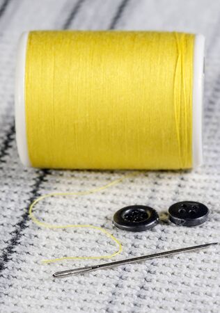 needle,buttons and yellow bobbin on knitting wool background.