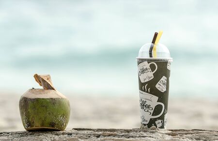 coconut and cup of cold coffee on decay timber at the beach.の写真素材