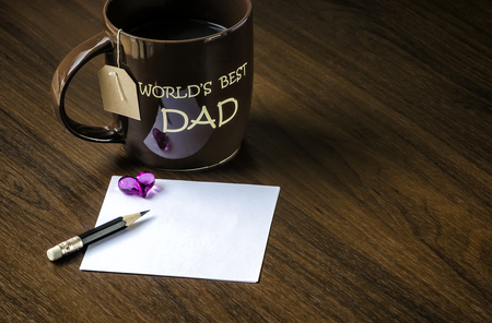 Brown cup of tea and blank white note on wooden tableの写真素材
