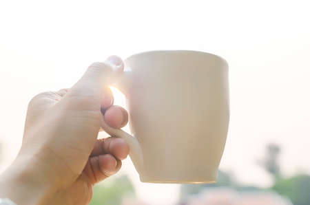 man hand holding cup of coffee against the sunlight in the morning,soft focus.の写真素材