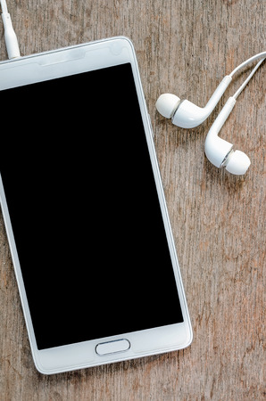 White smartphone with earphone on wooden background.の写真素材