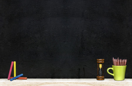 Green cup of pencils, hourglass and color chalks on the black board background.の写真素材