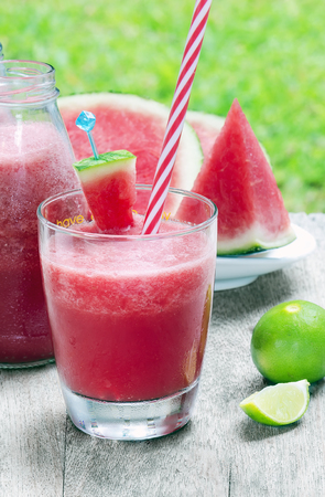 Watermelon juice and slices with lime on wooden table under nature light.の写真素材
