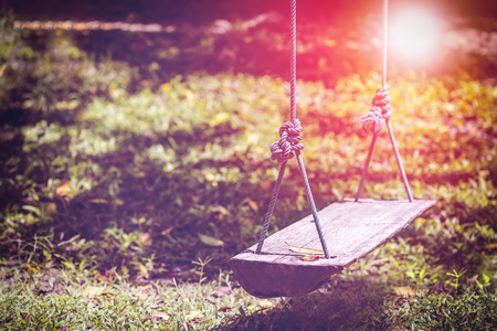 Old wooden swing hang in the garden under the sunlight.の写真素材