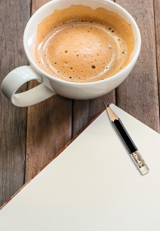 white cup of coffee and open blank notebook with pencil on wooden tableの写真素材