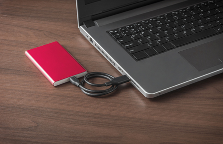 Red external hard drive connect to laptop computer on wooden tableの写真素材