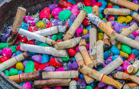 Lots of cigarette buds in a large ash tray with colorful stone